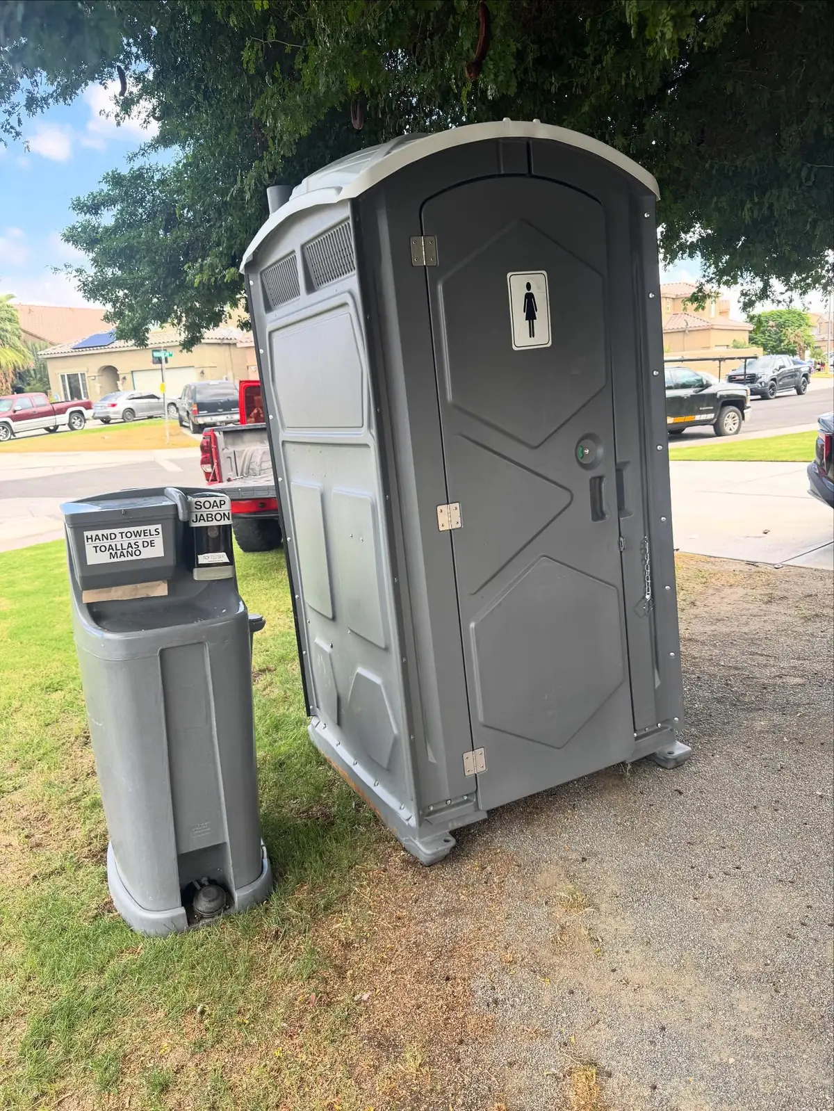 Gray portable toilet with a hand-wash station on grass